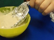 child hand lifting a liqued from a bowl with a foil spoon bending under the weight